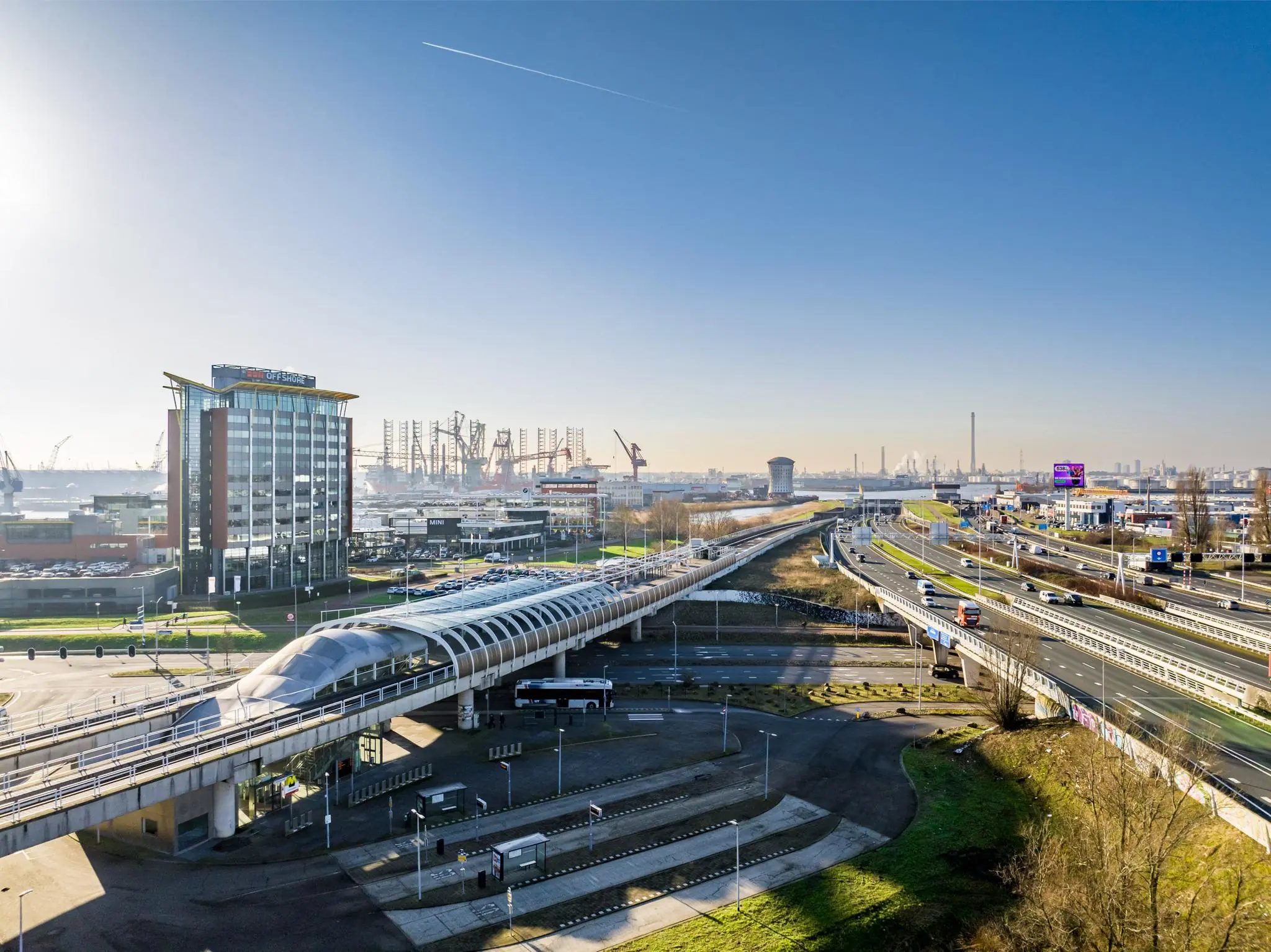 Luchtfoto van de Karel Doormanweg in Rotterdam met een modern OV-station, kantoren en de haven op de achtergrond.